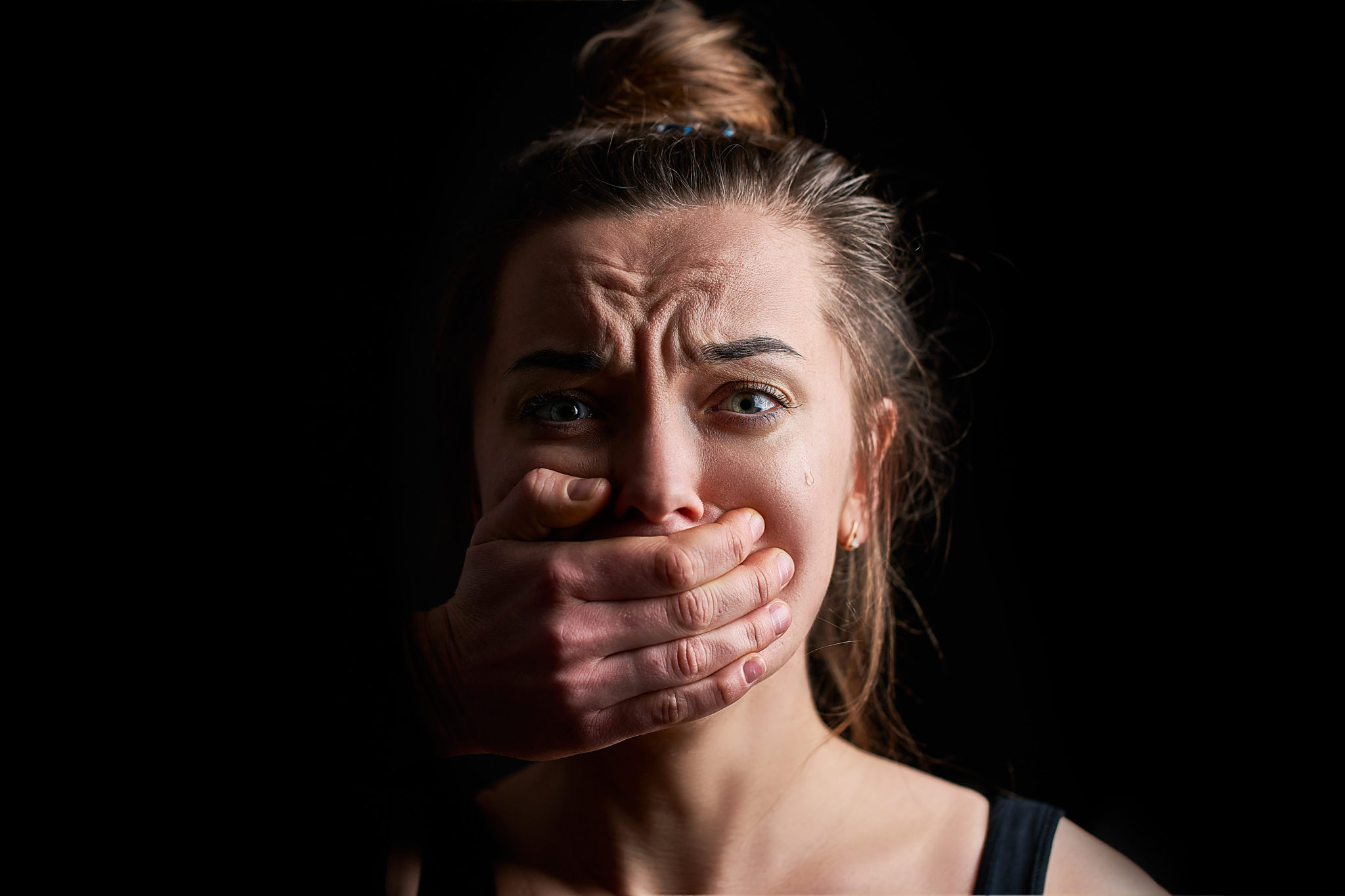 Stressed unhappy scared crying woman victim in fear with closed mouth on a dark black background suffering from domestic violence abuse