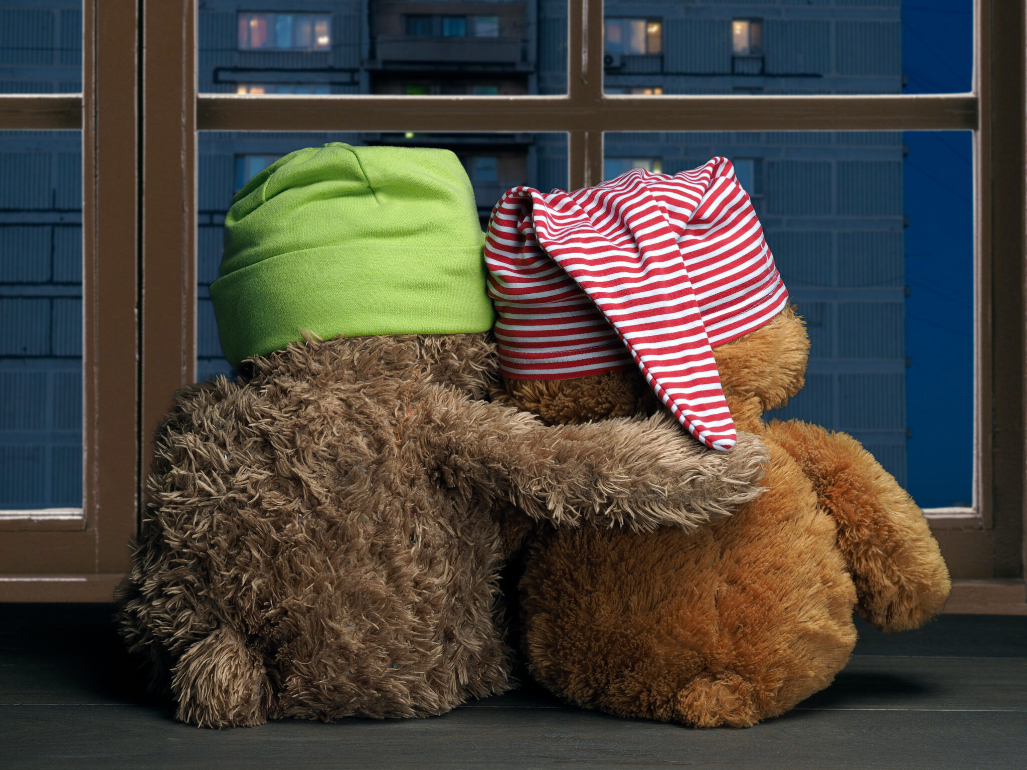 Two friends looking out the window at the windows of the house. Toys colorful hats bear cubs. Embrace the . Concept – love, friendship, support, evening together