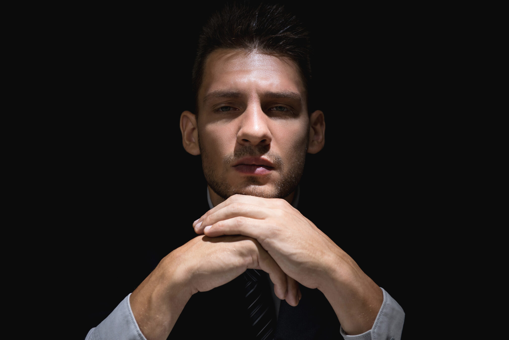 Pondering man in black suit with hands on chin in dark shadow